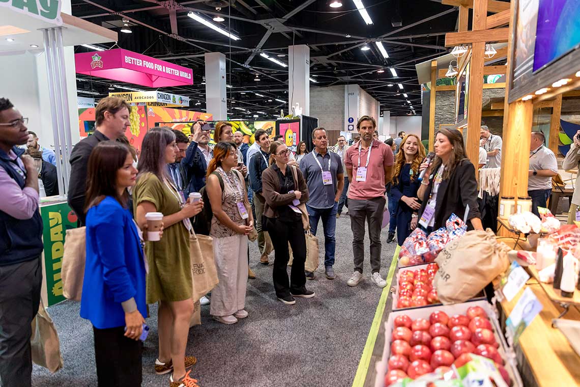 People at a GPFS 2025 listening to a speaker beside displays of produce.