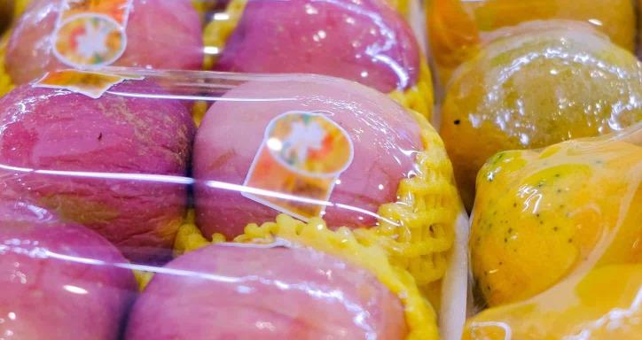 Assorted fresh fruits at market stall display wrapped in plastic film wrap for protection.