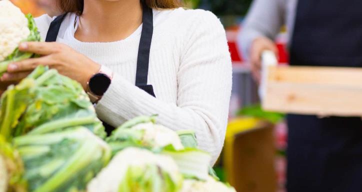 Latin saleswoman in black apron and her assistant with box of vegetables in background