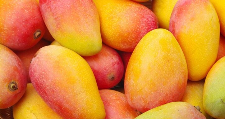 Close-up of ripe mangoes in a woven basket, with vibrant yellow and red skin.